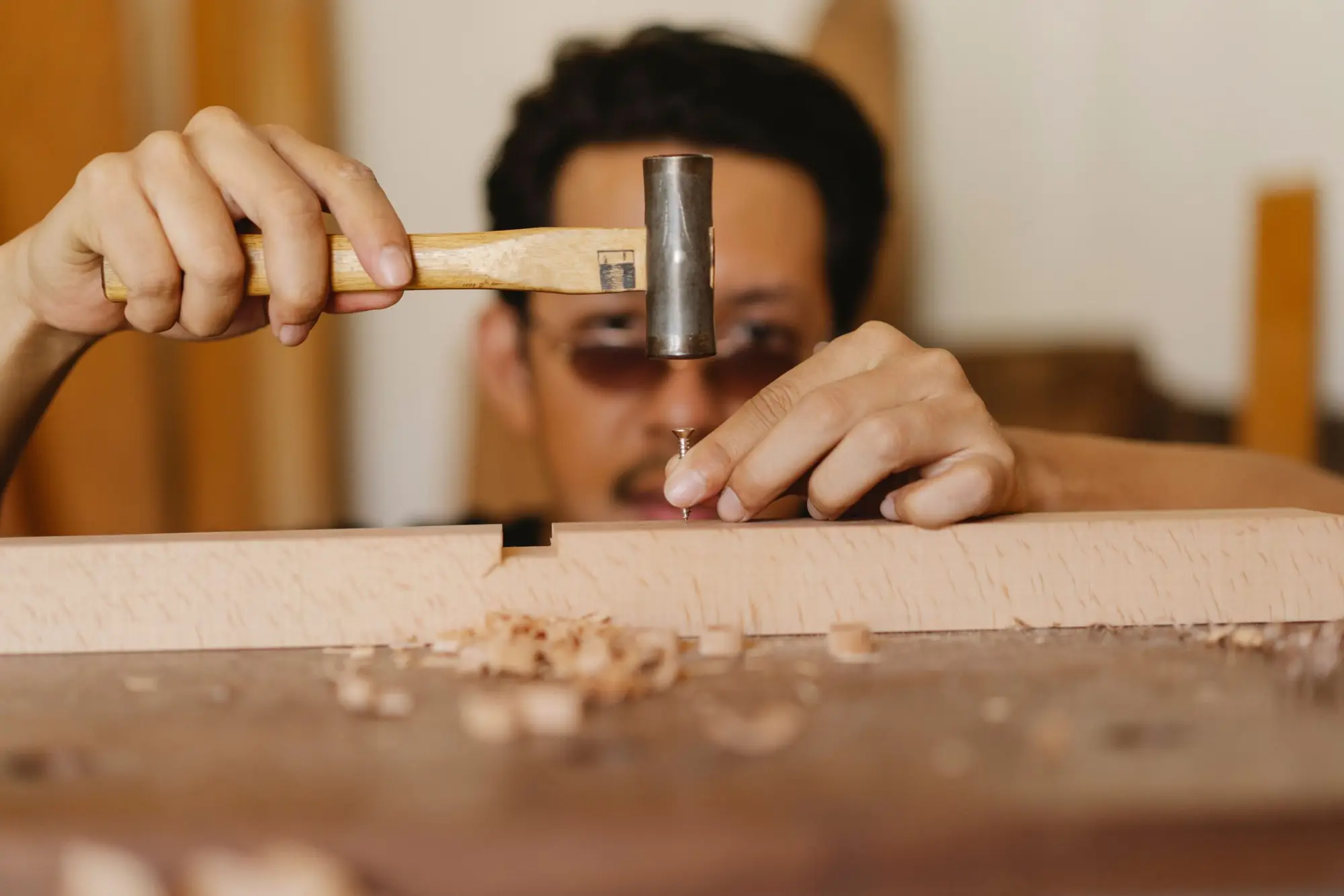 Woodworker tapping a fine nail into a timber board, with shavings on the bench
