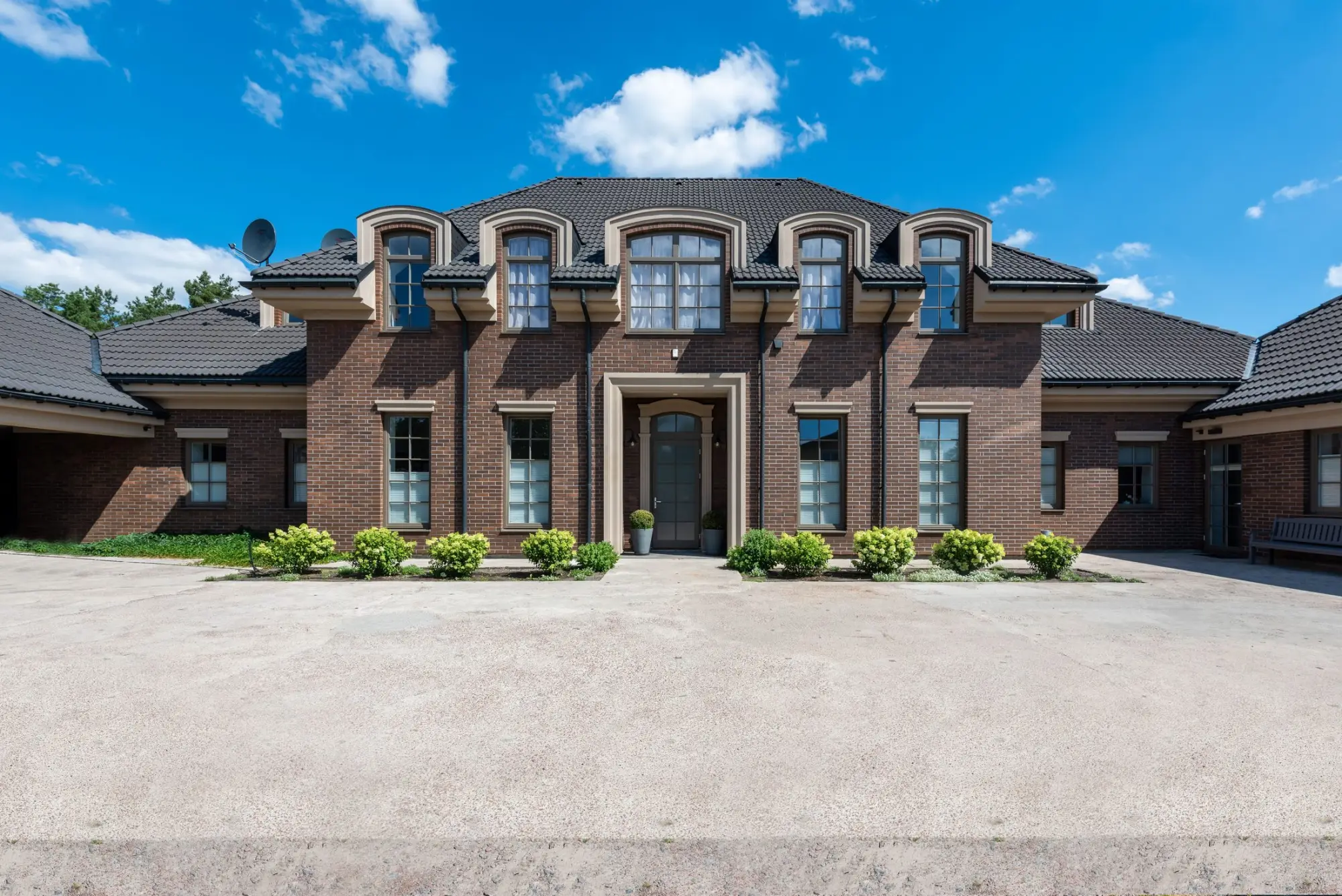 Two-storey red-brick home with arched dormer windows, a hipped roof and a wide forecourt