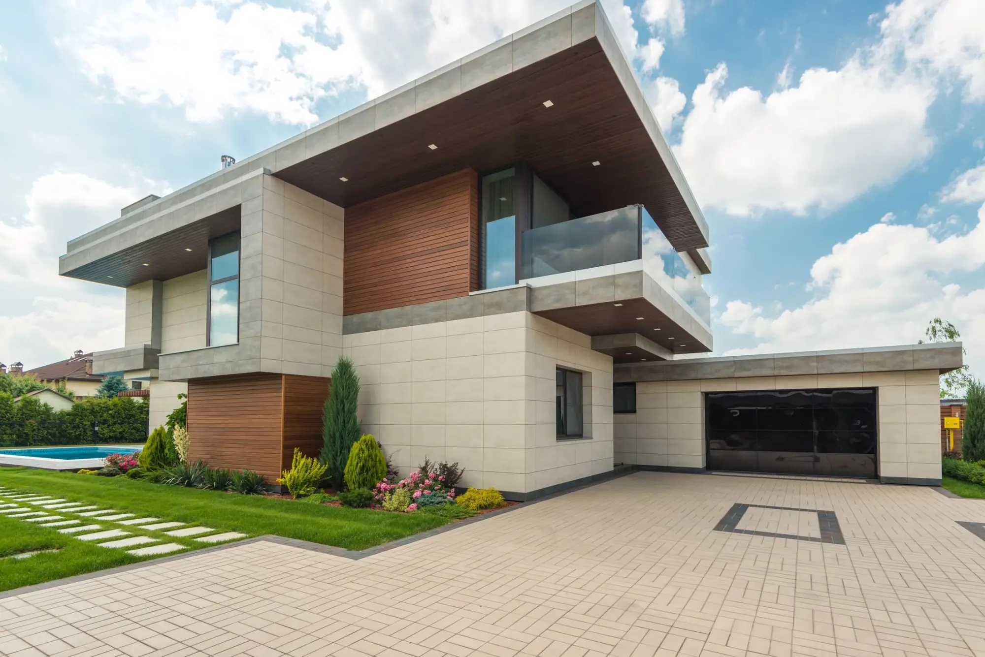 Contemporary home with cantilevered upper floors in pale stone and timber above a paved drive