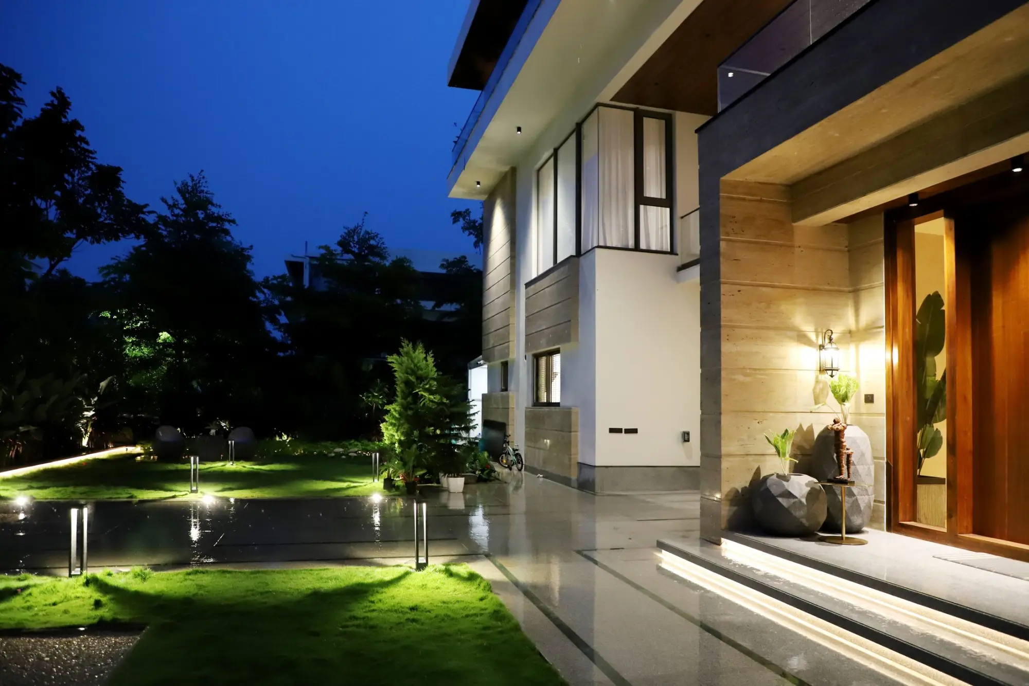 Contemporary house at night, its entrance and garden paths lit by low lights and a warm timber door
