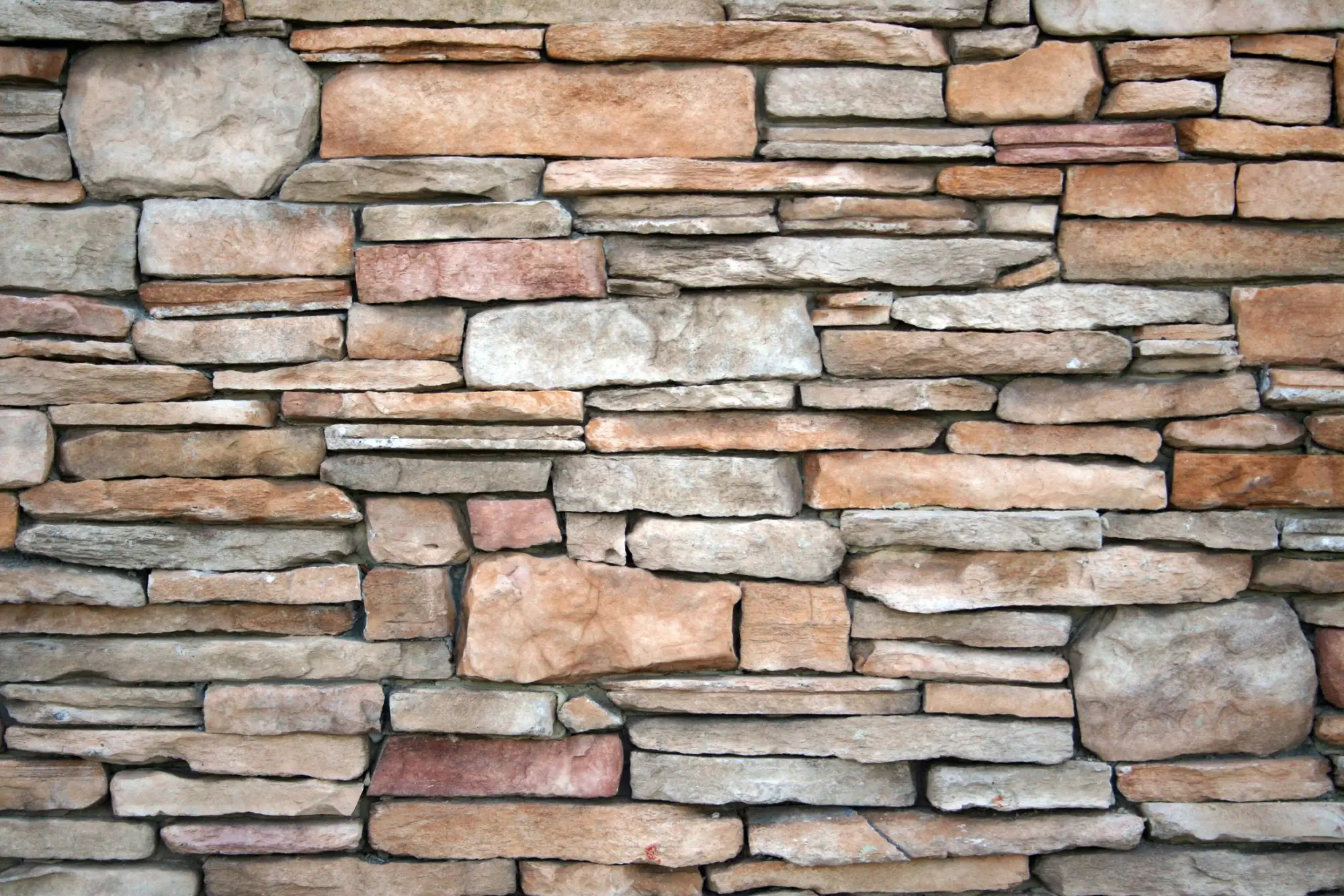 Close view of a dry-stacked stone wall in warm tan and grey tones