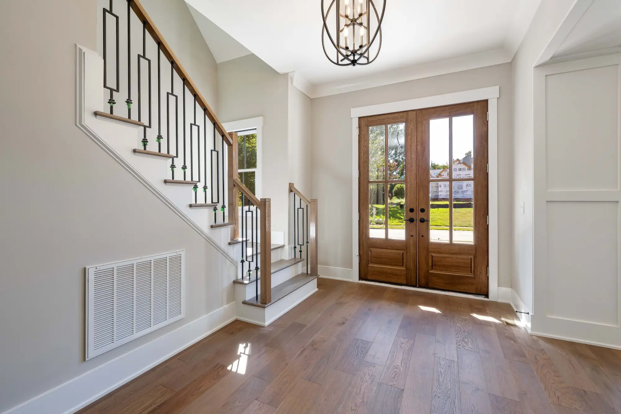 Bright entry foyer with an iron-baluster staircase, timber floors and glazed double doors